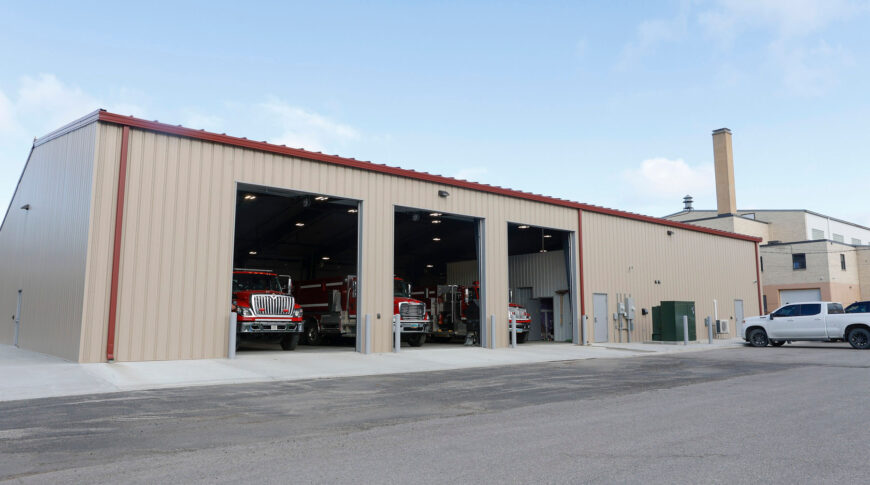 Bottineau Fire Hall - Low Res (17) Exterior of beige and red accented metal building with three large truck bays and fire trucks inside each one.