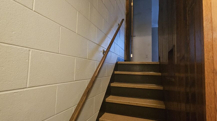 Dark stairwell with old brown stair treads and wood paneled walls before Comstock Construction remodel.