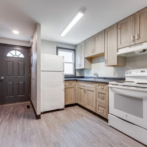 After renovation pictures of the townhome kitchen with new, lighter cabinetry and dark countertops, and gray LVP flooring.