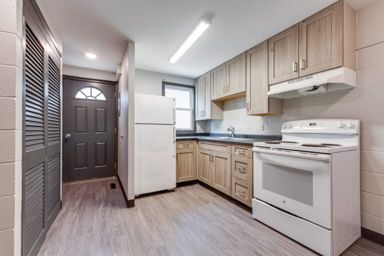 After renovation pictures of the townhome kitchen with new, lighter cabinetry and dark countertops, and gray LVP flooring.