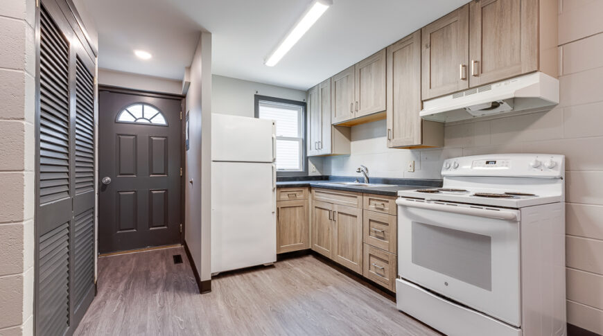 After renovation pictures of the townhome kitchen with new, lighter cabinetry and dark countertops, and gray LVP flooring.