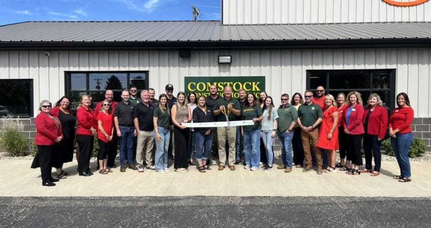 Group of Comstock Construction employees and Aberdeen Area Chamber of Commerce members congregate outside the Comstock Construction Aberdeen building holding a ribbon and scissors in hand for the official ribbon-cutting grand opening.