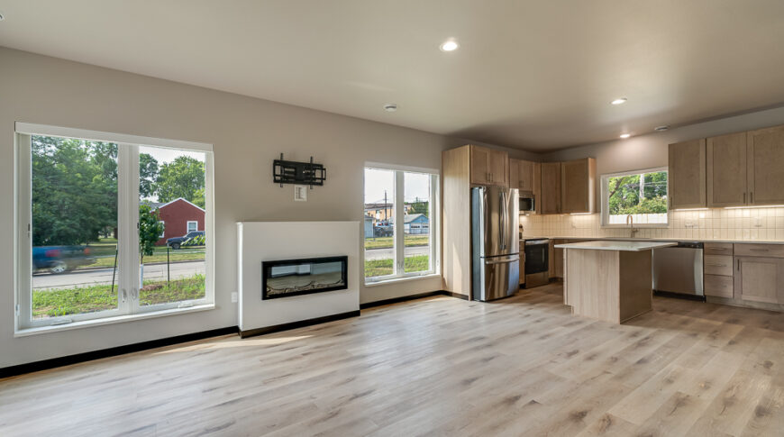 Bison Run Rentals - Low Res-14 Great room of Bison Lodge rentals showcasing a built-in fireplace feature flanked by two large windows and modern kitchen to the right.