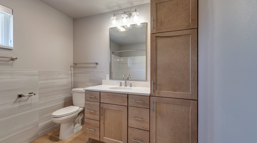 Bison Run Rentals - Low Res-22 Bathroom with light wood-toned cabinetry and flooring and light colored greige walls with tile accents on walls halfway up.
