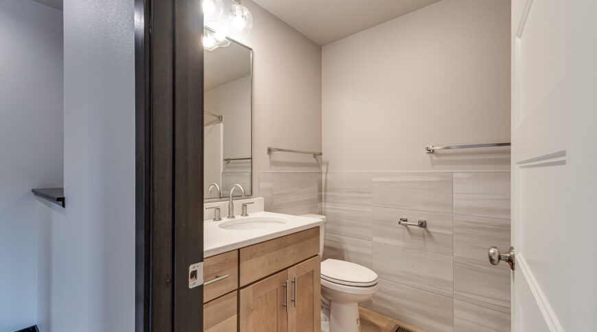 Bison Run Rentals - Low Res-27 Light and airy hallway bathroom with light wood vanity and flooring with light gray tiling halfway up the walls.