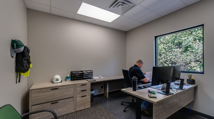 Comstock Construction Aberdeen-Low Res-44 Office with greige walls, light wood-toned cabinetry (only lowers), and a window overlooking green bushes.