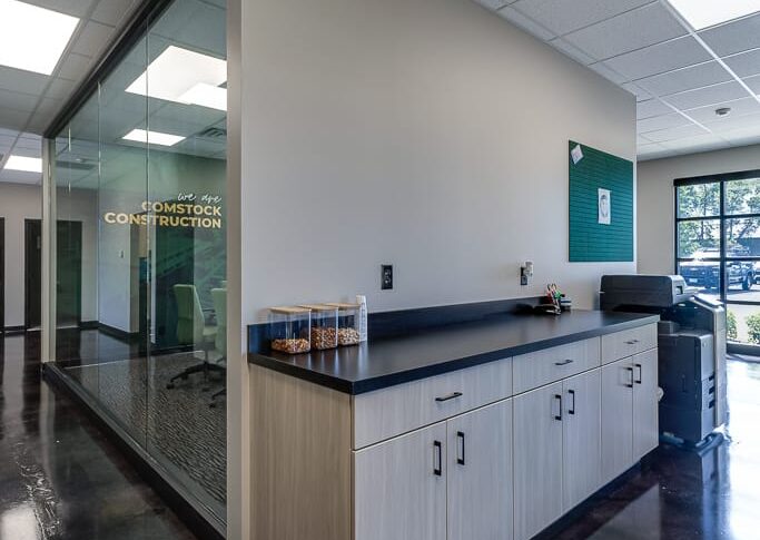 Comstock Construction Aberdeen-Low Res-49 Corner intersection of office with business station cabinets and printer to the right and wall of windows overlooking the conference room to the left.