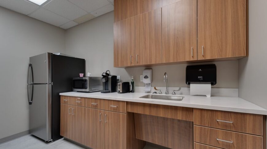 Sanford Hankinson-Low Res-23 Breakroom area with wooden upper and lower cabinets with sink, coffee machine, microwave and fridge.