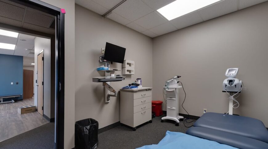 Sanford Hankinson-Low Res-33 Exam room at Sanford Hankinson Clinic with table and pillow in the middle of the room and wall-mounted tv monitor and some equipment besides.