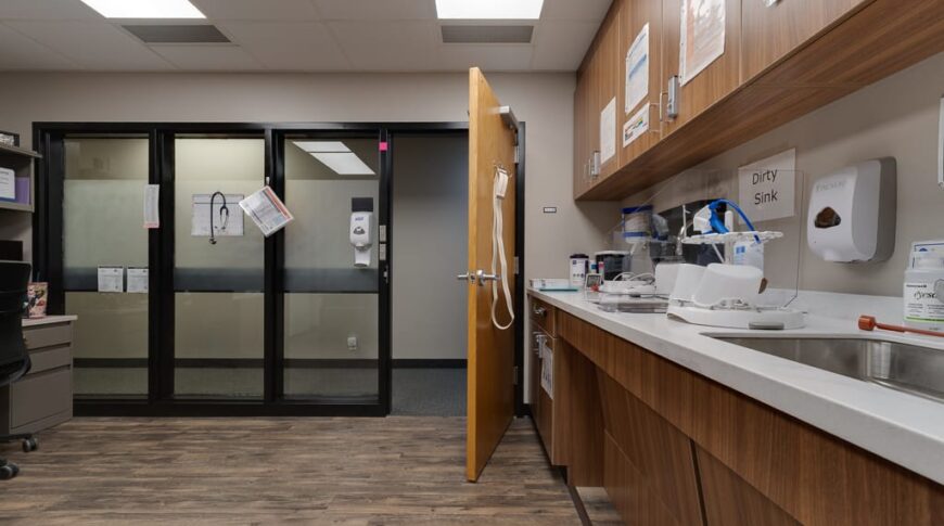 Sanford Hankinson-Low Res-51 Lab draw room at clinic with wall of cabinets with sink and supplies to the right and wall of windows and door to the back.