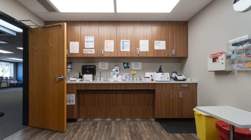 Sanford Hankinson-Low Res-52 Wall of wooden-colored cabinetry with a sink and lab equipment on the countertop, with LVP flooring at the lab room at Sanford Hankinson Clinic